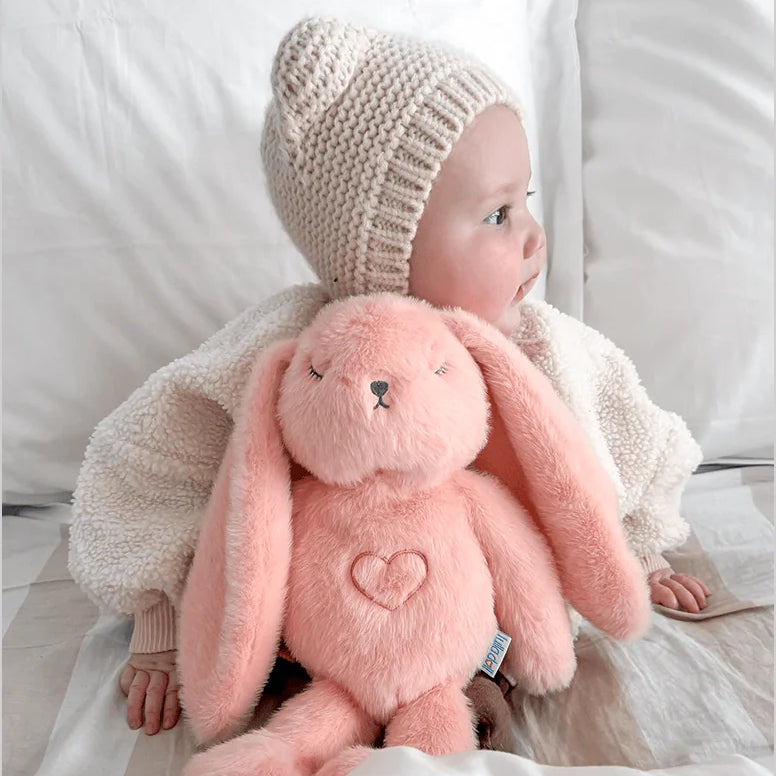 Baby holding a pink stuffed bunny toy with a white background