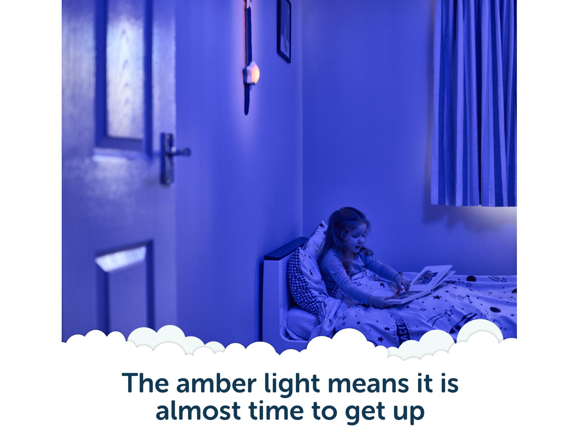 Child reading in bed with Rising Star glowing amber - almost time to get up.