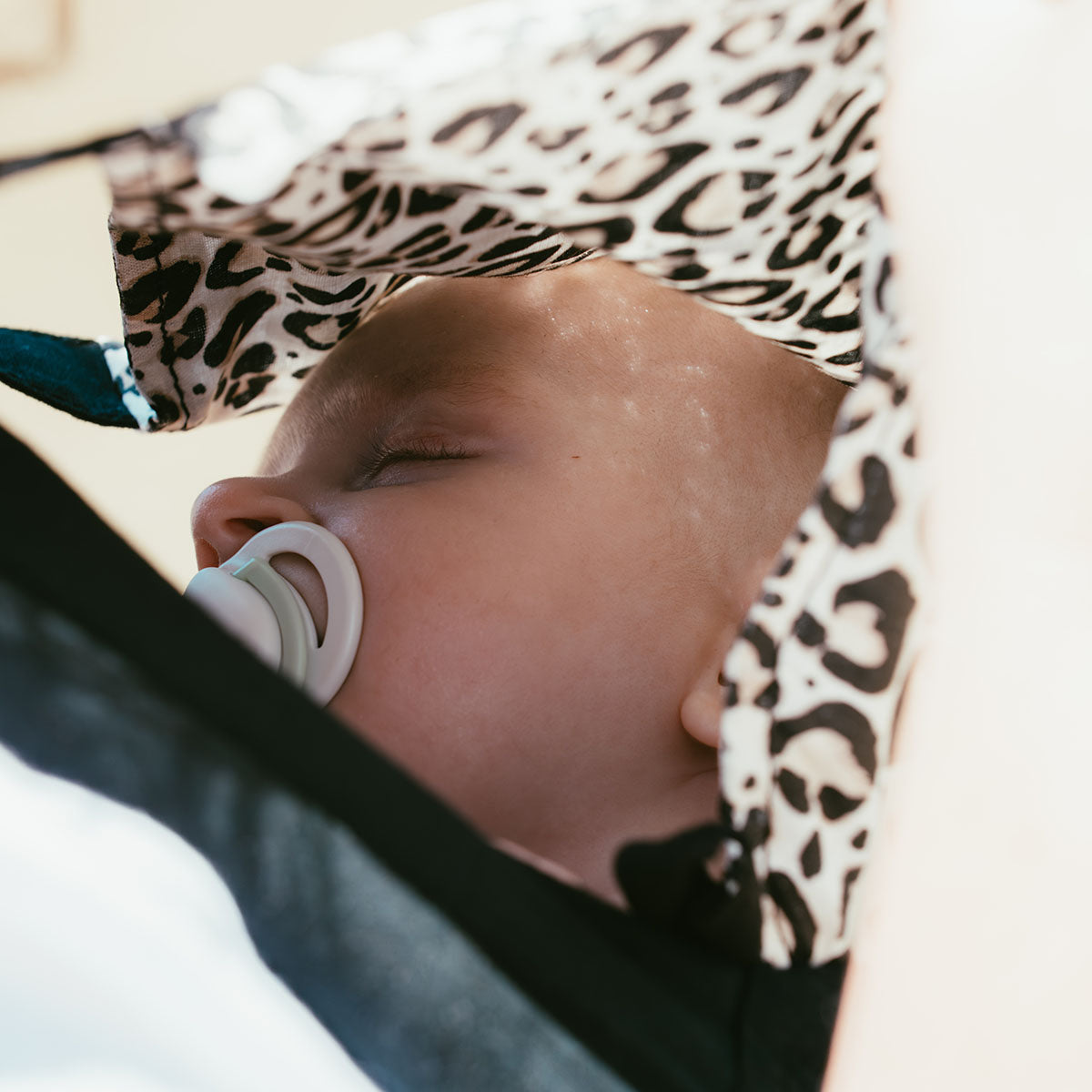 Baby sleeping under the leopard print hood of the Ubuntu Baba Stage 1 Wildling carrier