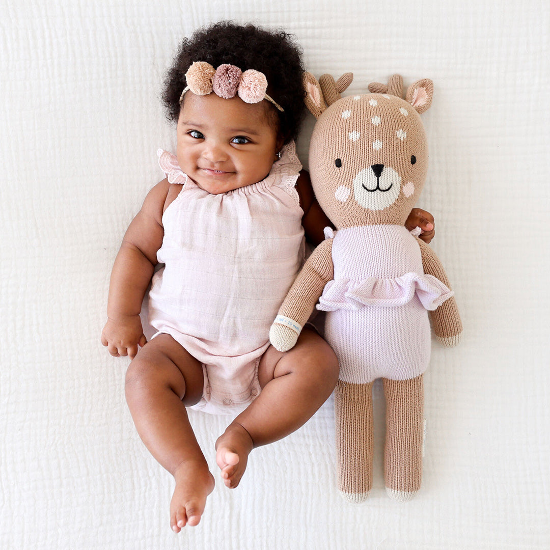A smiling baby with an arm around Violet the Fawn - Cuddle + Kind