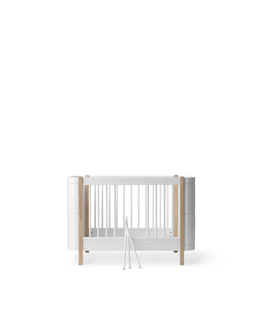 Wood Mini+ cot bed by Oliver Furniture in white and oak finish, showing the compact, modern design with slatted sides and sturdy frame.