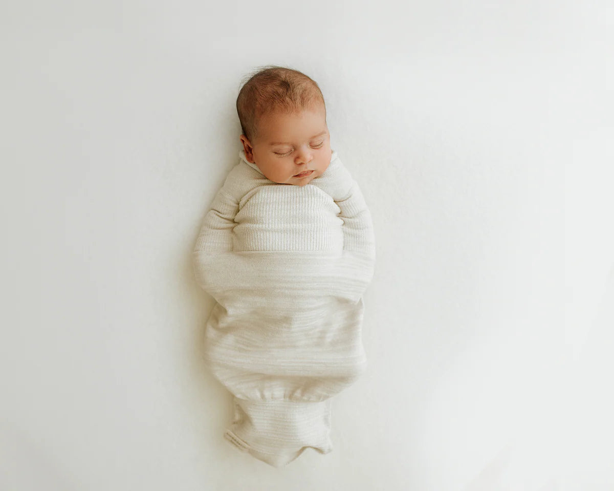 Newborn baby swaddled in a white blanket on a light background