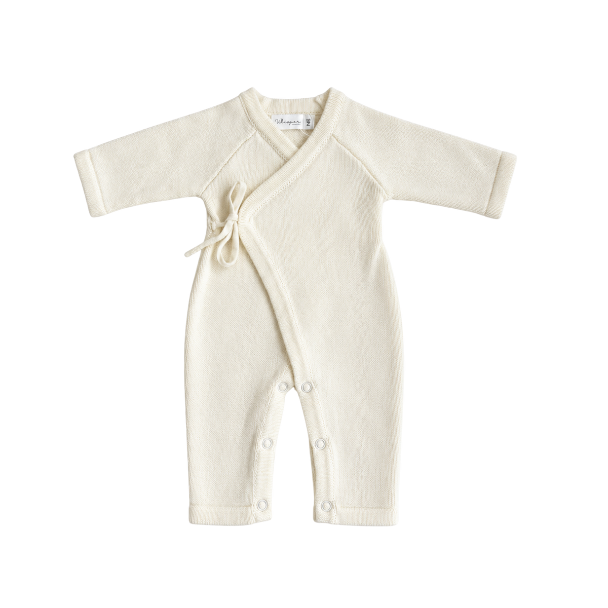 Baby girl wearing a cream knitted kimono romper from Bubbadue, with long sleeves and snap closures, lying on a soft blanket.