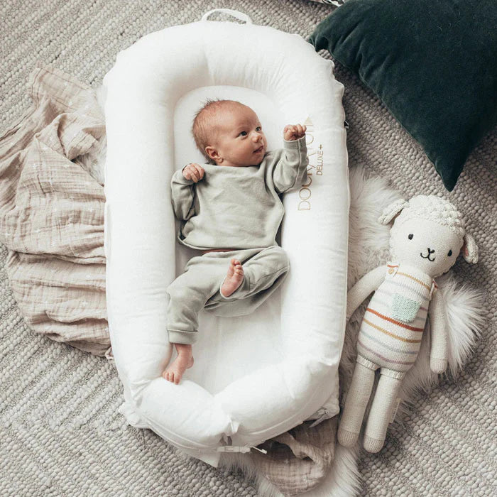 Pristine white Dock-A-Tot Deluxe+ Baby Dock for 0-8 months, showing soft fabric and cushioned design in a cozy nursery setting.