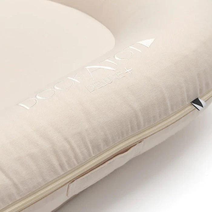 Dock-A-Tot Deluxe+ Baby Dock in Sand Chambray fabric, featuring soft, cushioned baby support for infants aged 0-8 months.