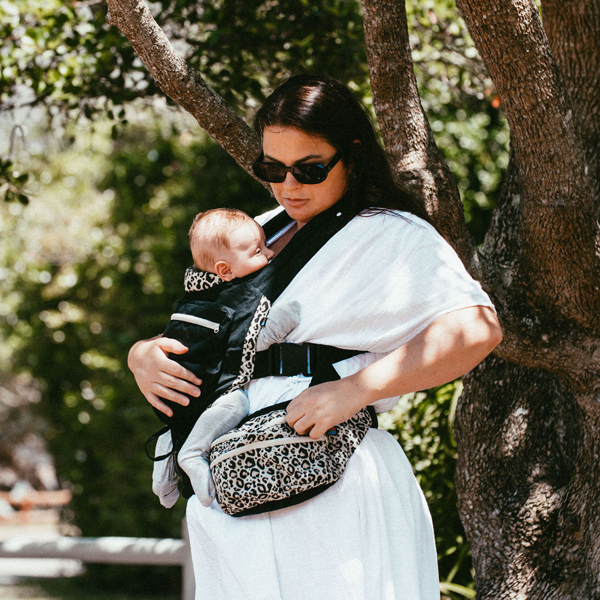 Ubuntu Baba Stage 1 Wildling baby carrier worn under a tree with baby resting on mom's chest